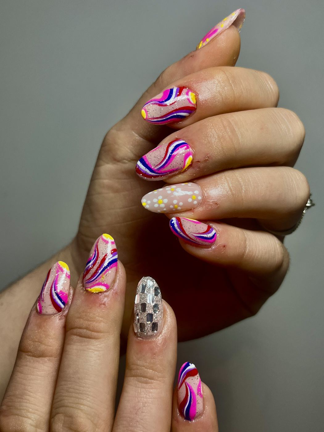 Nail art à volutes rose, rouge et bleu sur base nude
